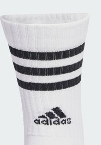 Calza sportiva bianca con strisce orizzontali nere e lavorazione a maglia testurizzata. Presenta il logo Adidas nero vicino alla caviglia.