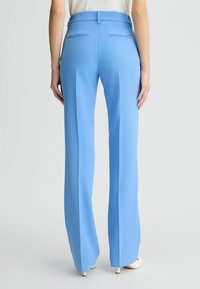 Pantaloni a vita alta e gamba larga in un tessuto azzurro chiaro. Presentano una trama liscia, tasche posteriori e pieghe sottili.