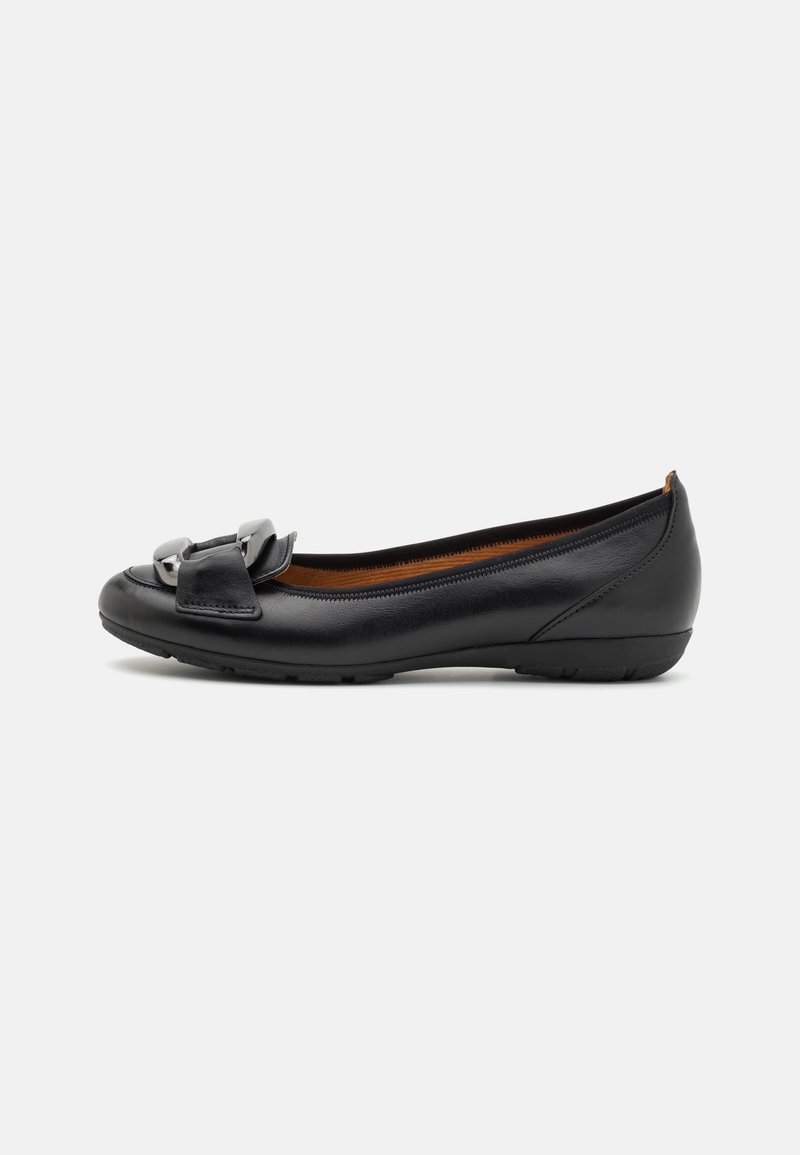 Chaussure plate en cuir noir avec un petit talon et un détail décoratif de boucle argentée à l'avant, vue de côté sur fond blanc.
