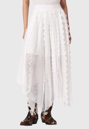 Valge asümmeetriline pitsseelik vertikaalsete sakiliste paneelidega, kantud musta-valgete mustriliste cowboy-saabastega.