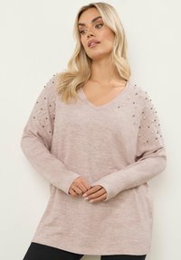 Vaaleanpunainen v-pääntie neulepaita, jossa on pitkät hihat, teksturoitu kangas ja koristellut olkapäät, joissa on erilaisia helmiä yksityiskohtia varten.