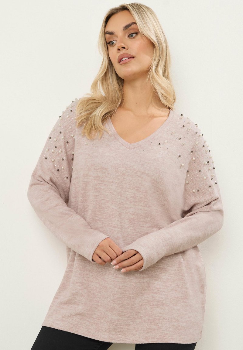 Vaaleanpunainen v-pääntie neulepaita, jossa on pitkät hihat, teksturoitu kangas ja koristellut olkapäät, joissa on erilaisia helmiä yksityiskohtia varten.
