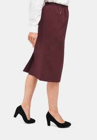 Bordeaux knielange rok met elastische tailleband, zijopening en een veilige ritszak. Gekenmerkt door zwarte suède hoge hakken.