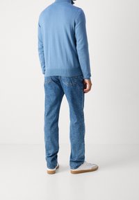 Pull-over bleu clair à col montant, associé à un jean bleu fuselé. Chaussures blanches avec des accents marron. Design minimaliste, look décontracté.