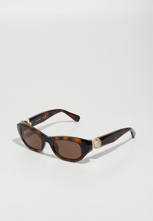 Schildpatt-Sonnenbrille mit braunen Gläsern, ausgestattet mit goldenen Beschlägen und einem Kristall-Akzent. Katzenaugenform und glatte Kunststoff-Oberfläche.