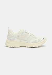 Sneaker atletico bianco con tomaia in rete, suola in gomma robusta, punta arrotondata e dettagli sottili lungo i lati. Presenti accenti testurizzati.