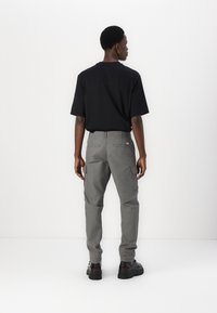 Pantaloni cargo gri, cu buzunare laterale și o croială relaxată, asortați cu un tricou negru cu mânecă scurtă. Material neted, design curat, culori neutre.