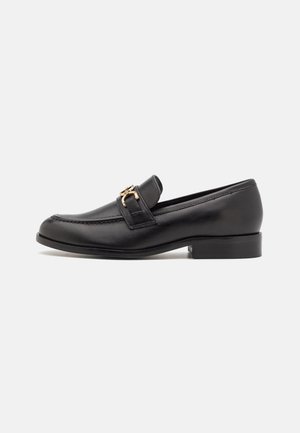 Black leather loafer with low heel and gold-colored metal buckle detail on side, shown in profile on white background.