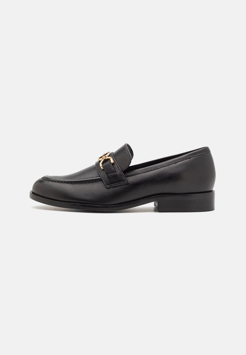 Black leather loafer with low heel and gold-colored metal buckle detail on side, shown in profile on white background.