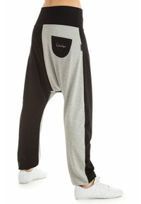 Sive in črne harem hlače z širokim pasom, ki imajo stransko žep in ohlapen kroj, izdelane iz mehke tkanine z gladko teksturo.