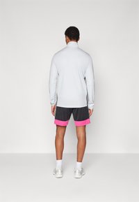 Lys grå langermet treningstopp med svarte sidestriper; kombinert med mørke shorts med rosa kant. Hvite sneakers fullfører antrekket.