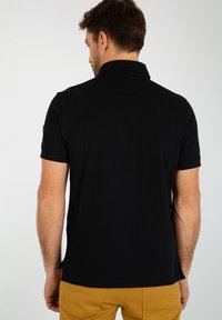 Zwarte polo met een klassieke kraag, korte mouwen en een licht gebogen zoom, gemaakt van zacht katoen. Bevat een logo op de linkerschouder.