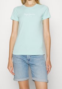 Mátová bavlněná trička s krátkým rukávem s bílým logem "Pepe Jeans London" na přední straně. Spárováno s ohrnutými denimovými šortkami.