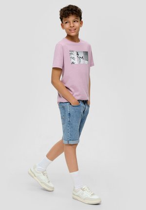 Lichtroze T-shirt met korte mouwen en grafische print, gecombineerd met denim shorts met opgerolde zoom. Sneakers met witte en crèmekleurige details.