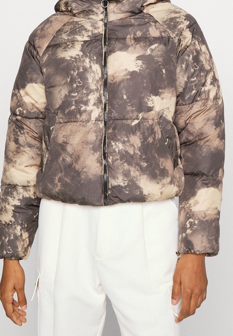 Doudoune à motifs tie-dye beige et gris, dotée d'une fermeture éclair à l'avant, d'une capuche et de poignets élastiques. Tissu doux et matelassé avec une coupe décontractée.
