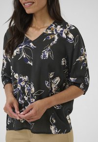 Blusa nera a fiori con scollo a V, caratterizzata da motivi crema, blu e marroni. Maniche corte a palloncino con polsini elastici; tessuto leggero.