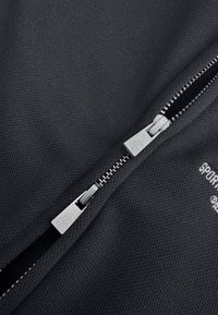 Zwarte stof met rits en een gestructureerd oppervlak. Zilveren metalen rits met zichtbare branding, die hoge contraststiksels langs de randen toont.