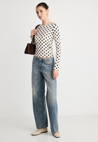 Pitkähihainen valkoinen paita, jossa mustia pilkkuja, yhdistetty vaaleansinisiiin, suoralahkeisiin farkkuihin. Malli pitää kädessään pientä tummanruskeaa käsilaukkua.