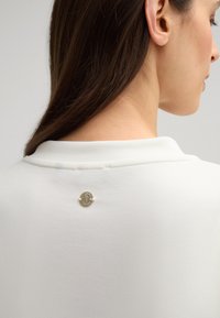 Witte sweatshirt met een gladde textuur, voorzien van een ronde gouden hardware accent aan de achterkant van de kraag.