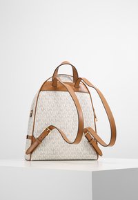 Rugzak van gemusterde beige stof met bruine leren accenten. Voorzien van verstelbare schouderbanden en een bovenhandgreep, met details in goudkleurig metaal.