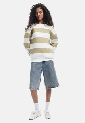 Sweter w paski w kolorze khaki i białym, z długimi rękawami i okrągłym dekoltem. Połączony z dżinsowymi szortami i białymi trampkami, w towarzystwie skarpetek za kostkę.