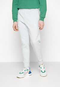 Light gray jogger pants with elastic waistband and cuffs, featuring a small white Nike logo. Paired with multicolored athletic shoes.