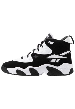 Scarpa atletica alta bianca e nera con chiusura a lacci e suola spessa e texturizzata, con un logo di marca prominente sul lato.