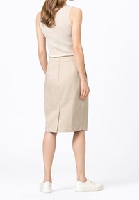 Gonna a matita beige con spacco posteriore, indossata sopra una canotta a coste leggera, abbinata a sneakers bianche. Presenta una vestibilità sagomata e una texture liscia.