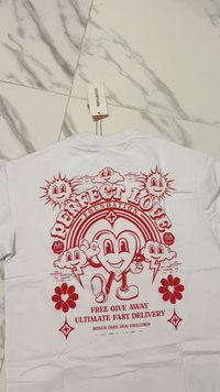Camiseta blanca de algodón con un diseño gráfico rojo de corazones sonrientes, nubes y flores, con el texto: "Fundación Amor Perfecto" y detalles del sorteo.