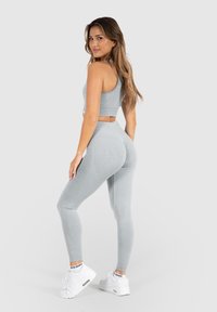 Grijze geribbelde crop top in combinatie met hoge, bijpassende leggings, voorzien van textuuraccenten en witte sportschoenen.