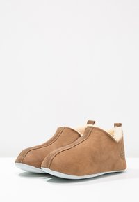 Chaussons en cuir suédé marron avec une doublure intérieure douce de couleur crème, design à bout arrondi et semelle en caoutchouc pour un usage intérieur.