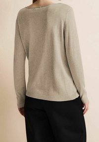 Light gray, long-sleeve sweater with a wide neckline, ribbed hem, and smooth texture; paired with black trousers in a neutral setting.