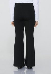 Schwarze, ausgestellte Hosen mit hohem Bund, aus einem elastischen Material gefertigt. Glatte Textur, minimalistisches Design und endet auf Knöchellänge.