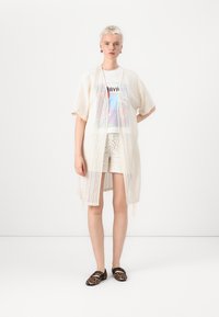 Kimono deschis, de lungime până la genunchi, țesut, de culoare crem, cu un model în zigzag. Asortat cu un tricou grafic și pantaloni scurți din croșet. Pantofi cu imprimeu de leopard.