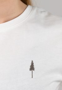 Witte katoenen T-shirt met een klein bruin geborduurd boomdesign aan de linkerkant van de borst. Zachte textuur, ronde halslijn, korte mouwen.