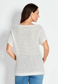 Witte gebreide top met korte mouwen, met een gestructureerd, open geweven patroon. Losse pasvorm, ronde halslijn en effen zoom. Gemaakt in combinatie met blauwe spijkerbroeken.