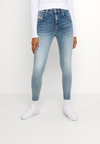 Tajta jeans i ljusblå denim med en blekt finish, som har framfickor och knappstängning, tillsammans med vita sneakers.