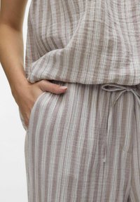 Ensemble sans bretelles, ample, en tissu doux et texturé, avec des rayures verticales beige clair et blanches, et une taille ajustable avec cordon de serrage.
