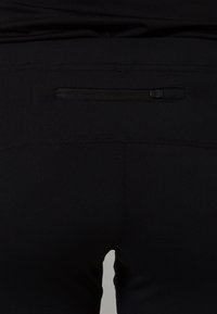 Black athletic pants with a fitted design, featuring a discreet zip pocket on the back and smooth, stretchy fabric.