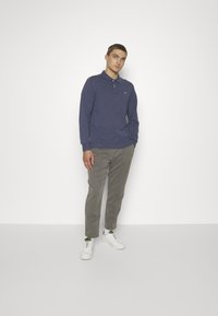 Langärmliges, marineblaues Poloshirt mit Kragen und Logo; kombiniert mit hellgrauen Hosen und weißen Sneakers mit grünen Akzenten.