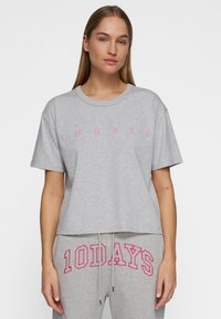 Camiseta gris corta hecha de una mezcla de algodón, con mangas cortas y texto impreso en rosa "10 DÍAS" en el pecho.