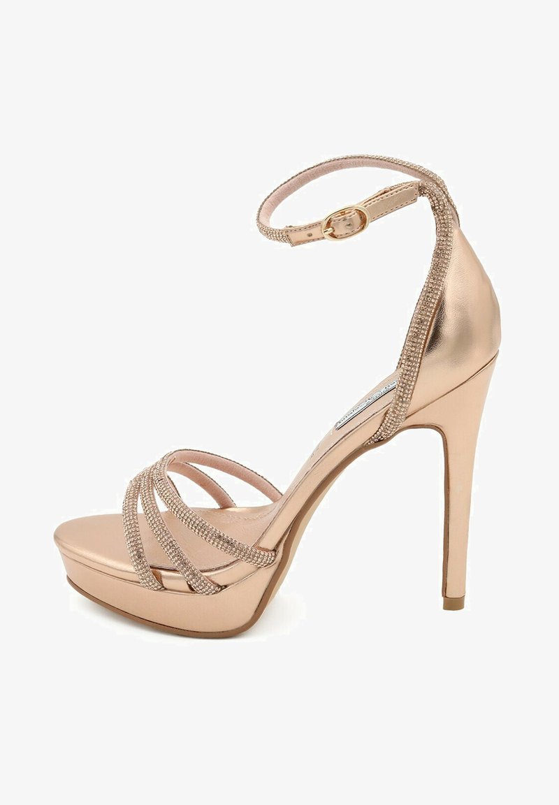 Sandalo con tacco alto in oro rosa metallico, dotato di cinturino alla caviglia, con bande incrociate luccicanti e suola a piattaforma per un'altezza extra.