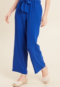 Blauwe, lichte, wijde broek met een textuurpatroon, voorzien van een tailleband met een strik. Gepaard met gevlochten espadrilles.