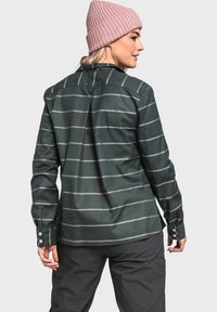 Tmavě zelená dlouhá košile s horizontálními šedými pruhy, s knoflíkovými manžetami a zadním skladem. V kombinaci s uhlově šedými kalhotami a světle růžovou čepicí.