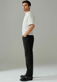Grijze T-shirt met korte mouwen, zwarte slim-fit jeans en zwarte schoenen. De outfit heeft een casual, ontspannen silhouet met een soepele textuur.