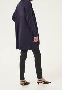 Fioletowy sweter rozpinany na drutach z wzorem w jodełkę, długimi rękawami i bocznymi rozcięciami, w połączeniu z czarnymi dopasowanymi jeansami i czarnymi, spiczastymi butami na obcasie z paskiem na pięcie.