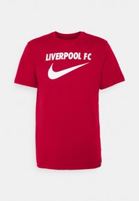 Punainen puuvillainen t-paita lyhyillä hihoilla, jossa edessä painettuna "LIVERPOOL FC" ja valkoinen Nike-logo. Yksinkertainen pyöreä kaula-aukko.