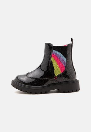 Bottine noire brillante avec semelle épaisse et panneau latéral élastique en maille arc-en-ciel colorée, présentée sur fond blanc.