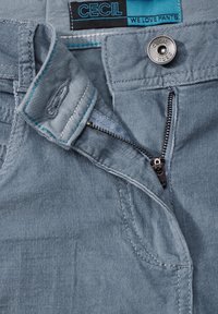 Ljusblå kordflortbyxor med detaljer som en dragkedja, metalldetalj och en tygetikett med texten 'CECIL' och 'VI ÄLSKAR BYXOR'.