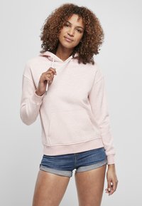 Világos rózsaszín kapucnis pulóver kenguru zsebből, állítható kapucnival és bordázott mandzsettával, farmer sorttal párosítva. Puha tapintású és laza kialakítású.